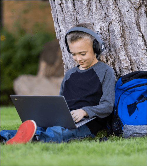 Student on laptop leaning on tree