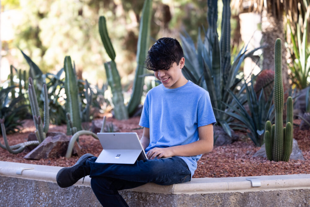 Estudiante de Poly sentado fuera con su portátil estudiando.